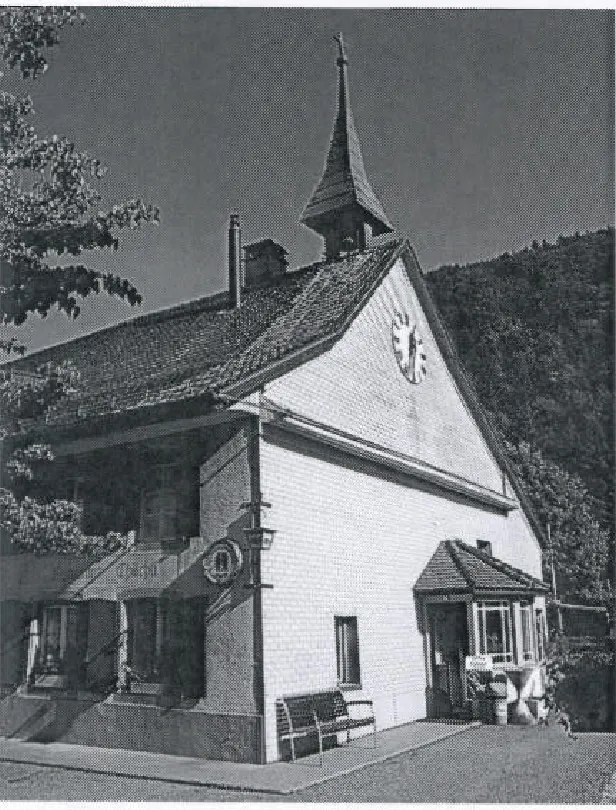 Das Chilchli in Bärenwil: Giebelfront mit Uhr, Dachreiter und Glocke vor dem bewaldeten Hang